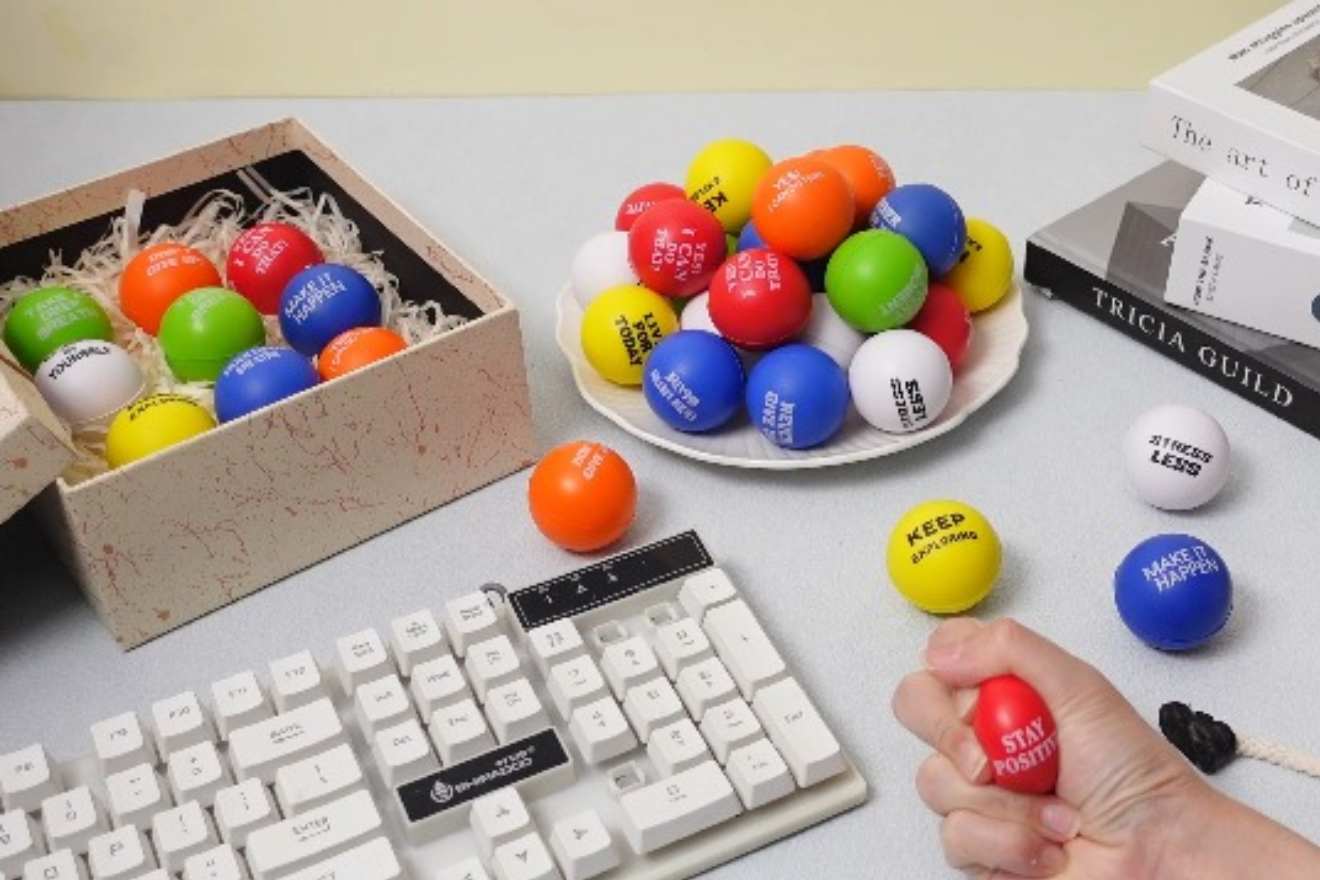 Person squeezing a custom yellow stress ball at office desk – personalized anti-stress products in various shapes and colors for branding and anxiety relief